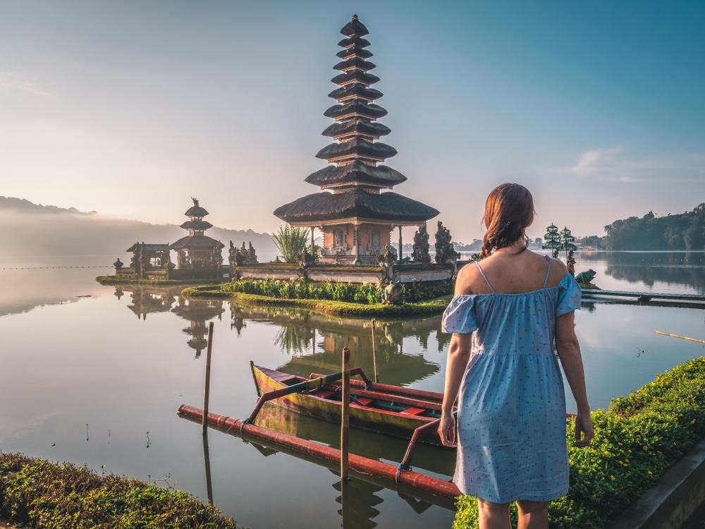 Young Woman Near Pura Ulun Danu Bratan Temple Near Beratan Lake In Bali Island, Indonesia At Sunrise. Iconic Image Of Bali And Southeast Asia. Travel And Adventure Background Image.